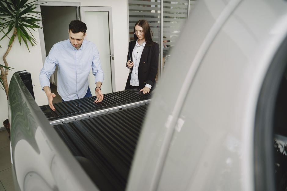 Salesman and client inspecting a pickup truck in a car dealership, discussing features.