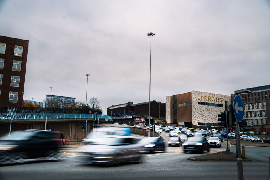 Dynamic scene of fast-moving vehicles at an urban intersection with a library in the background.